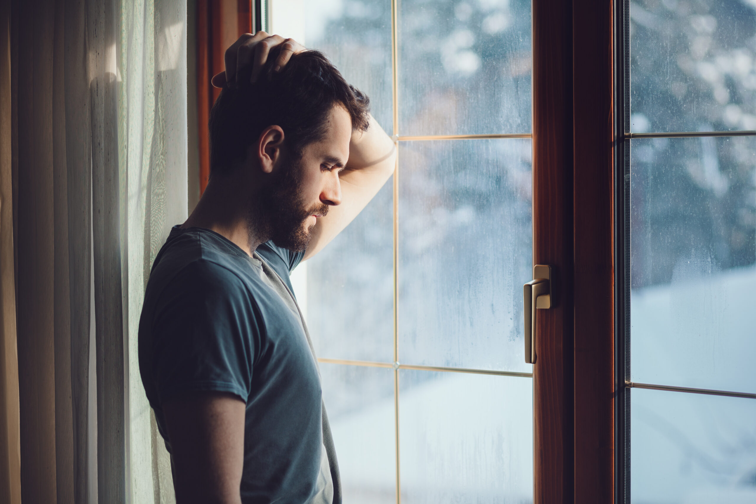 A man looks out a window, appearing sad or frustrated.